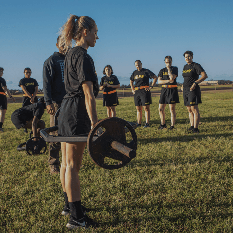 Female soldier prepares for deadlift as others watch during morning ACFT.
