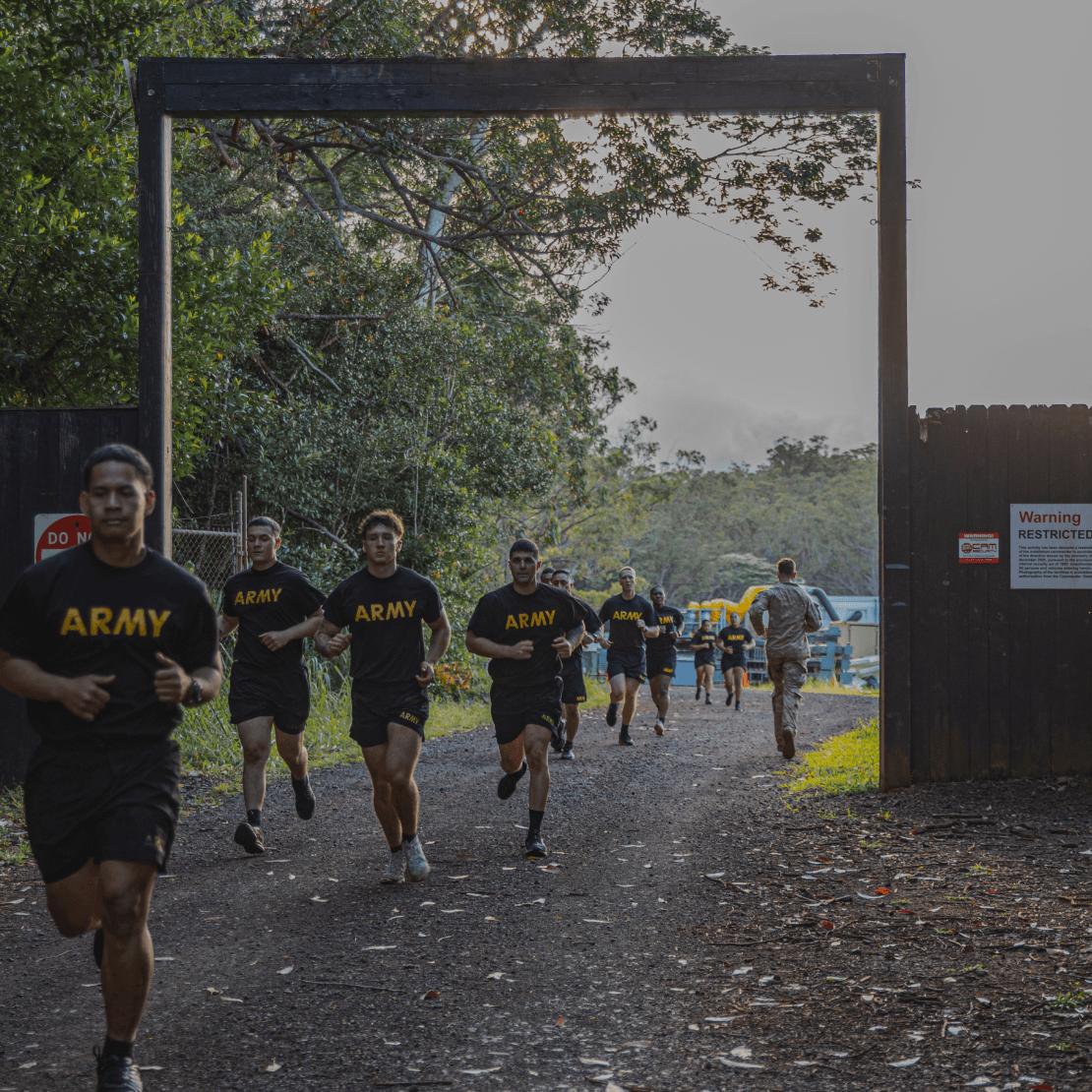 Group of soldiers running through a gate during the two-mile run in a wooded area.