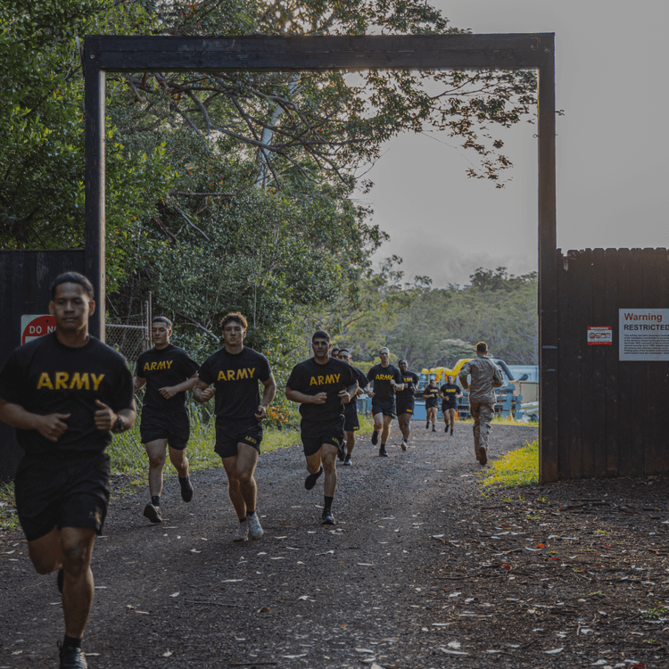 Group of soldiers running through gate during ACFT endurance test in wooded area.