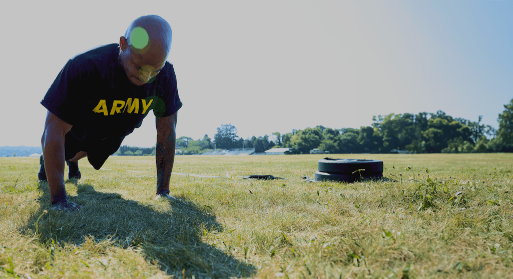 Soldier performs hand-release push-up for ACFT scoring on sunny field, showcasing Army fitness.